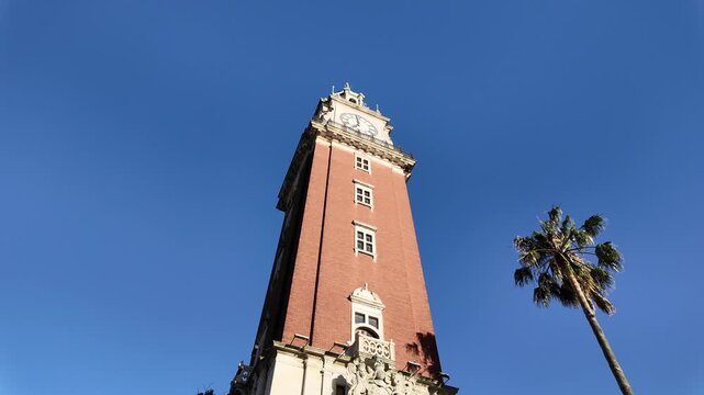 Close-up of the Monumental Tower from its brick base up to the large clock and bronze dome under the blue sky at sunrise in Buenos Aires Argentina.
