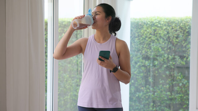 Young gen z active woman drink whey creatine shake bottle eating diet food using phone calorie plan app after home sport workout. health care asia people happy relax protect aging life weight loss.