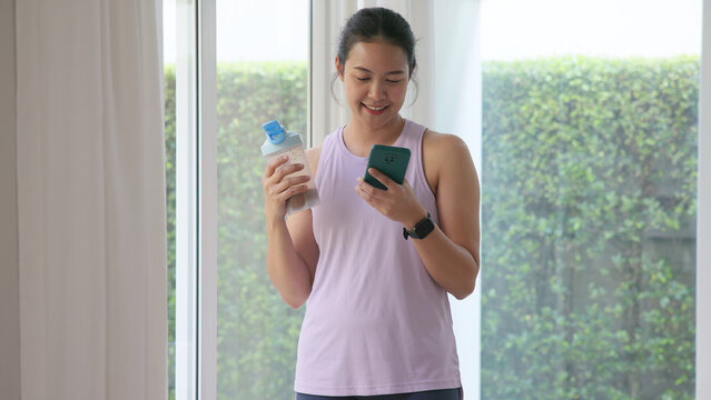 Young gen z active woman drink whey creatine shake bottle eating diet food using phone calorie plan app after home sport workout. health care asia people happy relax protect aging life weight loss.