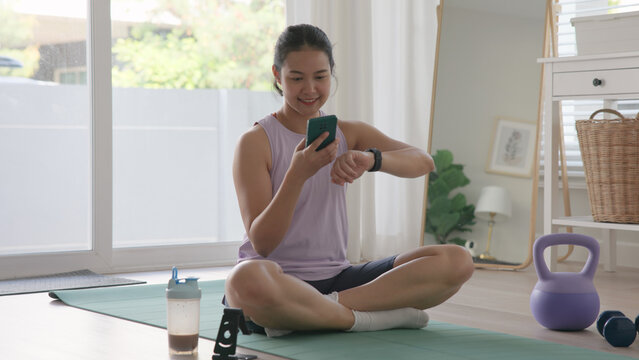 Young active Gen Z woman using smart watch phone wrist wear check app heart rate zone AI report after home workout Health care internet of things asia people happy cheerful anti aging life weight loss