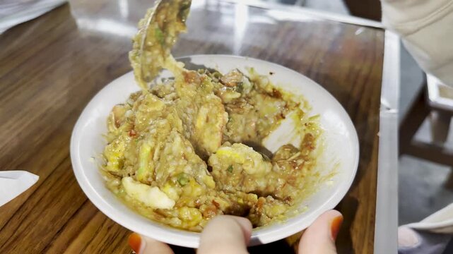 A close up horizontal video of stirring a warm bowl of chicken porridge or bubur ayam, blending together the savory rice congee, shredded chicken, and aromatic toppings.