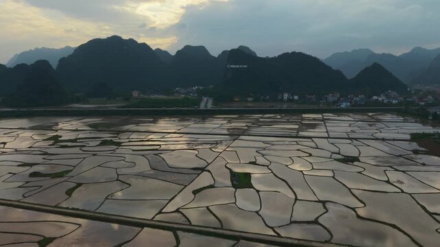 Aerial Flooded Rice Fields At Sunset, Reflective Water Mirrors Karst Mountains And Distant Village, Tranquil Rural Panorama In Phong Nha Vietnam Captured By Drone, Golden Light, Calm Mood