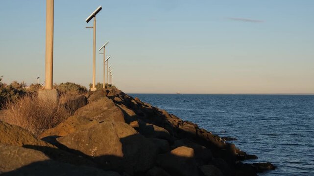 A rugged basalt rock breakwater at Werribee South wit solar-powered street lamps. Long stone barrier stands against the sea waters of Port Phillip Bay, Melbourne Australia.
