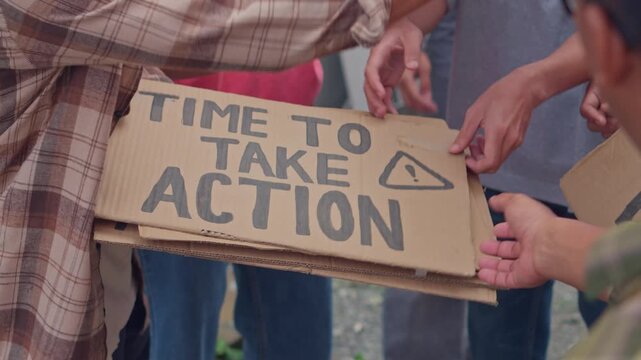 Group of diverse activists share and distribute various handmade cardboard protest signs for rally