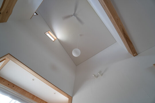 High Ceiling Interior With White Plaster Walls And Ceiling Fan（大きな窓と吹き抜けがあるナチュラルな雰囲気の日本の一軒家のリビングの天井）