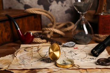 Treasure map with travel equipment, hip flask and smoking pipe on brown wooden background © Pixel-Shot