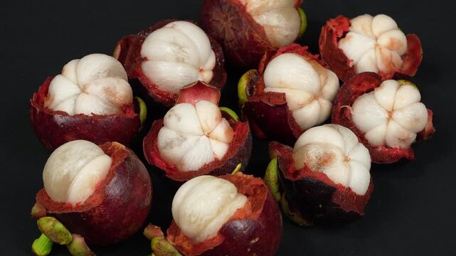 A cinematic macro loop video of many opened purple mangosteen fruits spinning on black background.
