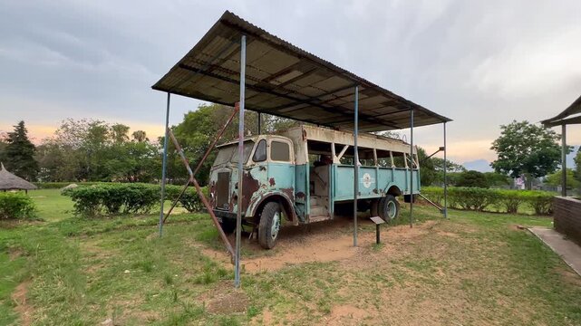 An old, weathered bus stands under a corrugated roof amidst green surroundings in Blantyre, Malawi. Ideal for historical or cultural projects.
