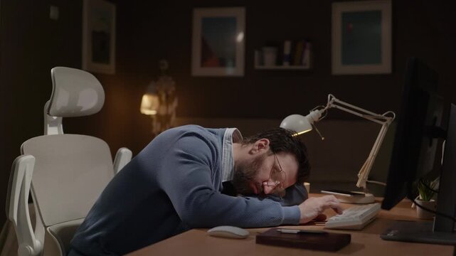 Tired freelancer. Exhausted remote worker sleeps at his computer desk, reflexively tapping his finger on keyboard. Burnout, fatigue, deadline, sleep deprivation concept