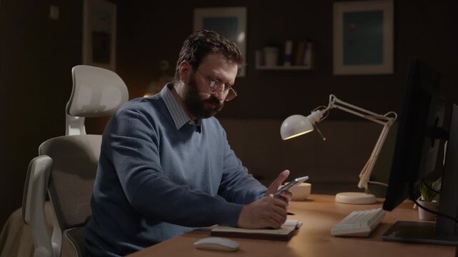 Freelancer at work, planning, preparing concept. Male freelancer working remotely takes notes in diary, uses phone and computer