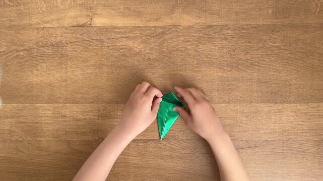 Child Hands Folding Shiny Green Origami Paper from an Overhead View, 4K Slow Motion Silent Video