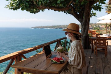 Obraz premium Woman with laptop working remotely at seaside table overlooking ocean travel