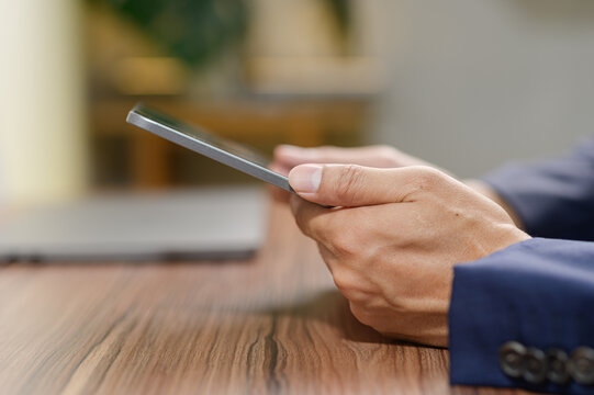 Hands Holding Smartphone Close-Up on Wooden Table in Office Environment