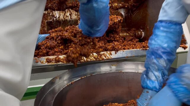 Worker removing prepared food filling from an industrial mixer after the mixing process. Ingredient handling procedure supporting batch production, product consistency, and efficient food manufacturin