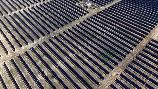 Drone video showcases a vast solar power farm with orderly, endless rows of gleaming photovoltaic panels in bright daylight, emphasizing renewable energy and modern infrastructure.
