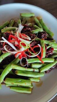 Close-up video of spicy stir-fried long beans with beef slices, garnished with red chili and spring onions. Delicious Asian cuisine with vibrant colors and rich texture, perfect for restaurant, culina