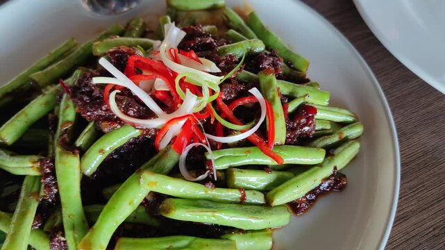 Close-up video of spicy stir-fried long beans with beef slices, garnished with red chili and spring onions. Delicious Asian cuisine with vibrant colors and rich texture, perfect for restaurant, culina