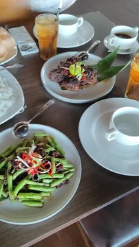 Overhead moving camera shot of an Asian dining table featuring multiple traditional dishes, iced drinks, soup, rice, and crispy meat presentation. Cinematic restaurant atmosphere with aesthetic food a