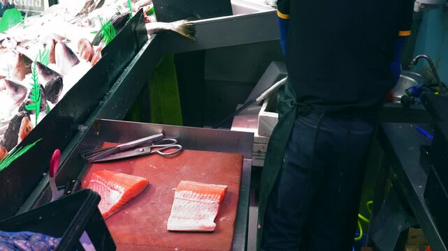 Professional fishmonger cutting and preparing a fresh salmon fillet on a cutting board at a market