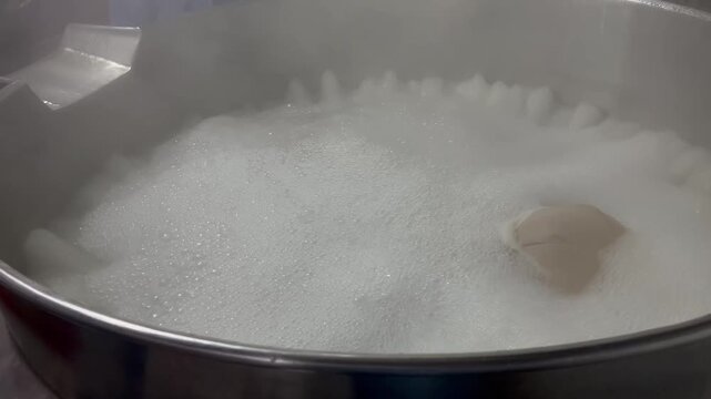 Large quantities of garlic boiling in an industrial cooking kettle during Bak Kut Teh broth production. Food manufacturing process used to prepare soup base for large-scale food production and ready m