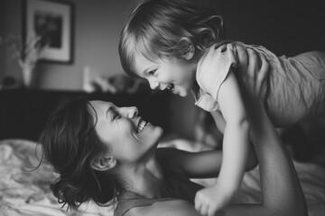 Fototapeta premium Black and white portrait of a joyful mother lifting her laughing toddler child on bed