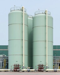 Obraz premium Mint green industrial storage tanks standing in a production facility with pipe manifold networks for clean energy, sustainable industry and engineering concepts