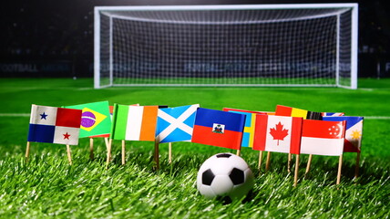 Small national flags of different countries arranged in a row on a green grass soccer field with a ball in front of a goal net © Photo Agency