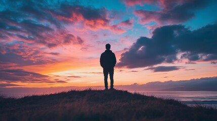 Obraz premium Silhouette against a fiery sunset, peaceful horizon with clouds above a grassy hill