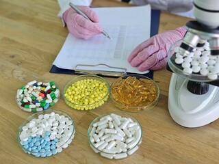 Scientist examines pills and capsules while taking notes © Nadzeya