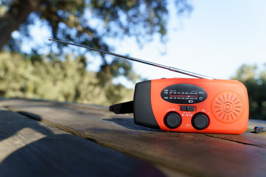 Orange hand crank radio with antenna on a wooden table, receiving essential information during outdoor activities or emergencies