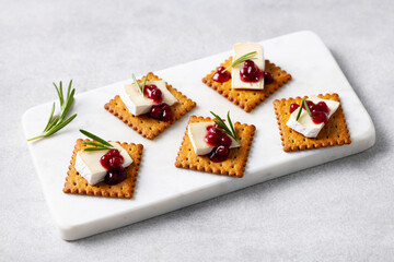 Fototapeta premium Crackers with brie cheese cranberry sauce and fresh rosemary on white marble board. Grey background.