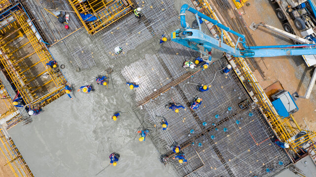 Construction Site Aerial View: An aerial perspective of a busy construction site where workers in yellow hard hats pour concrete, showcasing industrial progress and development.