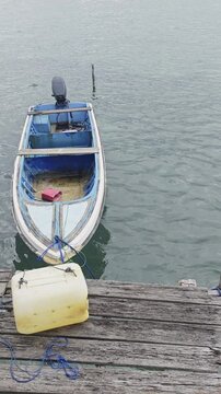 a small blue motorboat moored to a wooden dock on calm sea water