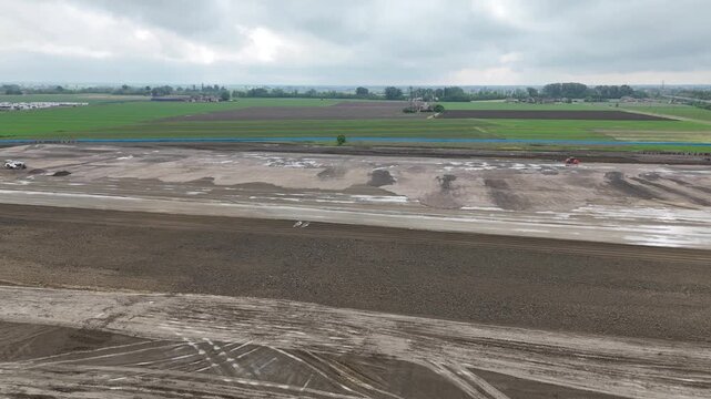 Large earthmoving and grading operations for datacenter construction across agricultural plain in northern Italy, with leveled soil, heavy machinery tracks and infrastructure development, aerial drone