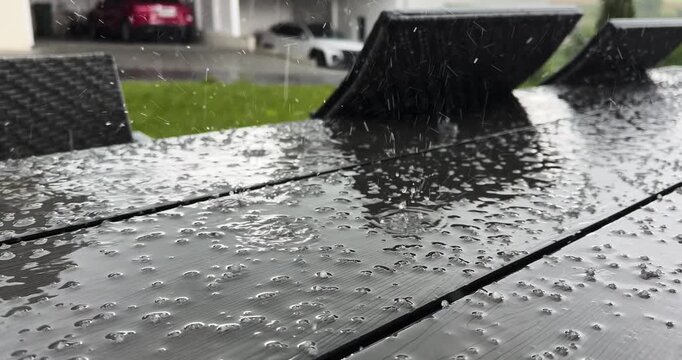 hailstones and rainwater hitting a dark outdoor terrace table during a storm, showing severe weather, sudden hail, garden furniture, climate impact, property risk, and summer storm atmosphere.