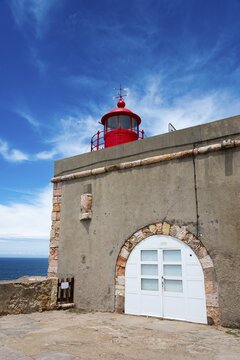 Round red lighthouse on a beige building with stone accents and blue sky in the background, Fort S&atilde;o Miguel Acanjo, Farol de Nazar&eacute;, lighthouse of Nazar&eacute;, S&iacute;tio, Sitio, Nazar&eacute;, Nazare, Oeste, district Leiria, Centro, Estremadura, Portugal