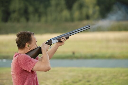 An old man shoots from a hunting rifle at a shooting range. Smoke from the barrel is visible in the frame