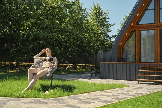 A woman in a swimsuit sunbathes on the lawn of a country house on a warm weekend