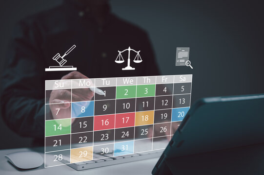 Person interacts with digital calendar interface featuring legal icons above workspace manage court dates schedule appointments during busy day in corporate office setting.