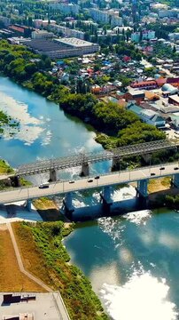 Vertical video. Yelets, Lipetsk region, Russia. Karakum automobile and pedestrian bridges spanning the Sosna River, Drone footage over the historic city center under a bright summer sky. Drone footag