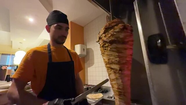 Male chef cooking and slicing doner kebab meat at a restaurant