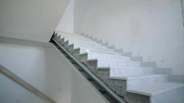 Stone staircase winds upward between plastered walls in building under renovation. Clean surfaces show early stage of building project