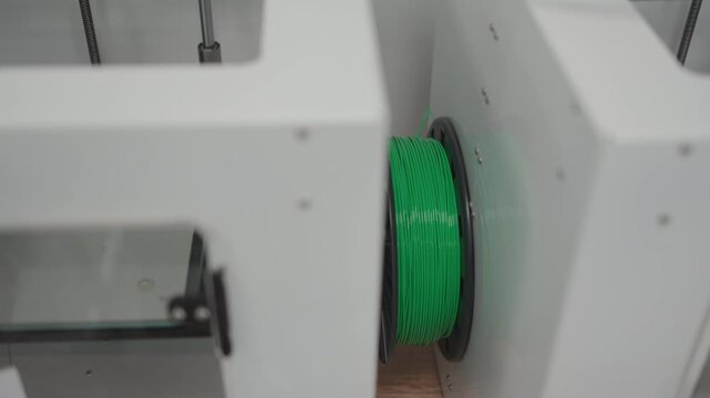 Modern additive manufacturing machinery features clean metal chassis. Vibrant plastic material spool awaits digital prototyping process