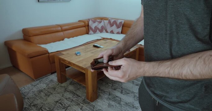 man checking an empty wallet in a living room, representing financial stress, lack of money, low budget, cash shortage, personal expenses, and cost-of-living pressure.