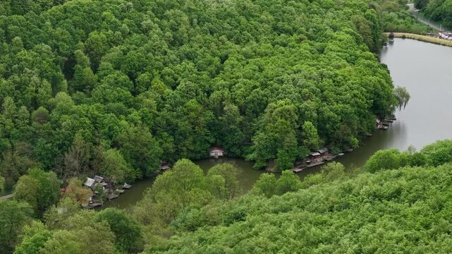 An aerial view shows small rustic cabins tucked along the banks of a winding river surrounded by a lush forest.