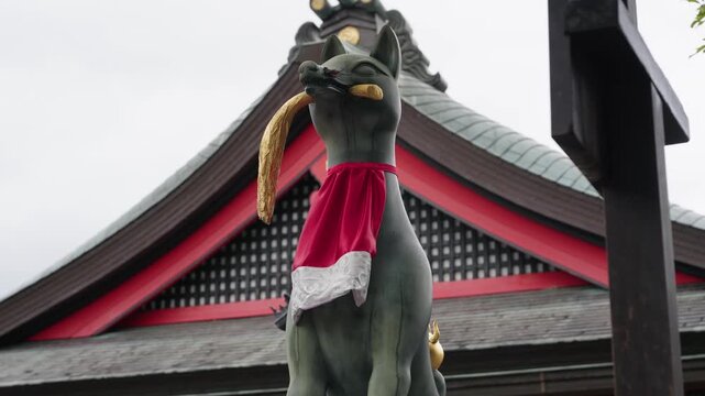 Stone kitsune fox statue holding golden key in mouth with red bib against shrine roof at Fushimi Inari Kyoto