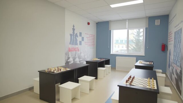 Modern classroom features tables with chess sets near large bright window. Clean organized space feels welcoming and peaceful for students