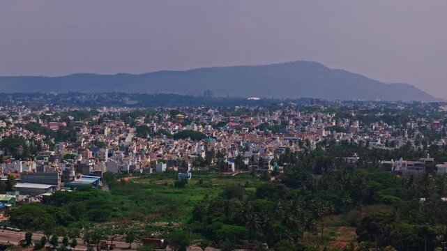 Cityscape with Chamundi hills, haze, trees and moving vehicles on road at Mysuru, karnataka, india. day time, semi circle shot, drone shot, 4k.
