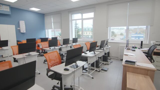 Spacious educational laboratory workspace includes teacher desk and multiple computer setups. Wide windows let light into clean room