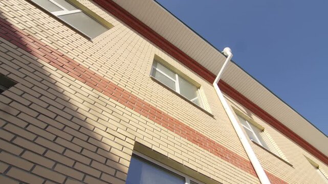 Stainless steel rain gutters run down yellow and red brick facade. Bright daytime sunshine illuminates clean modern architecture